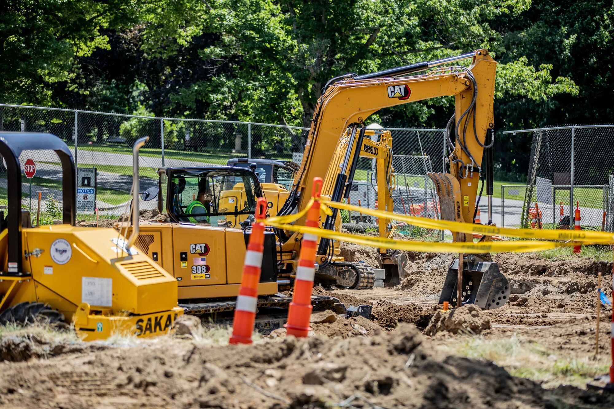 A line of Caterpillar excavators working an open excavation on a fenced federal campus