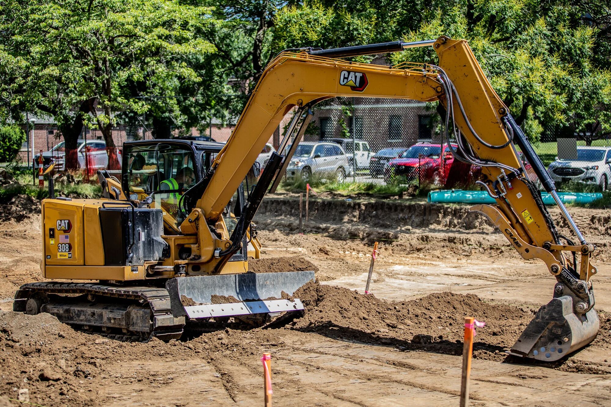 An excavator cutting a deep trench beside a completed section of sitework