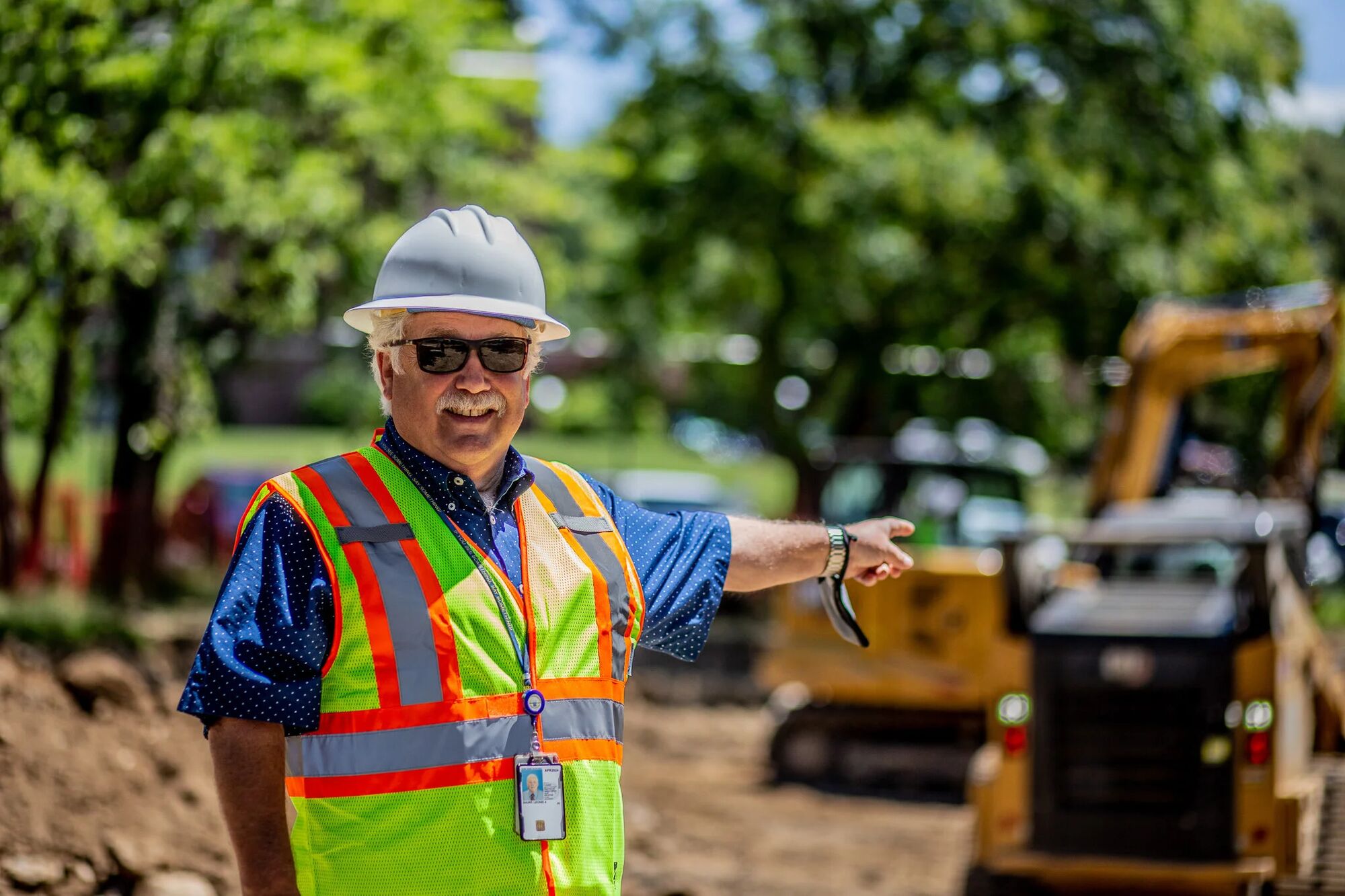 An Industry Standard USA foreman in a hard hat and high-visibility vest standing at an active excavation site