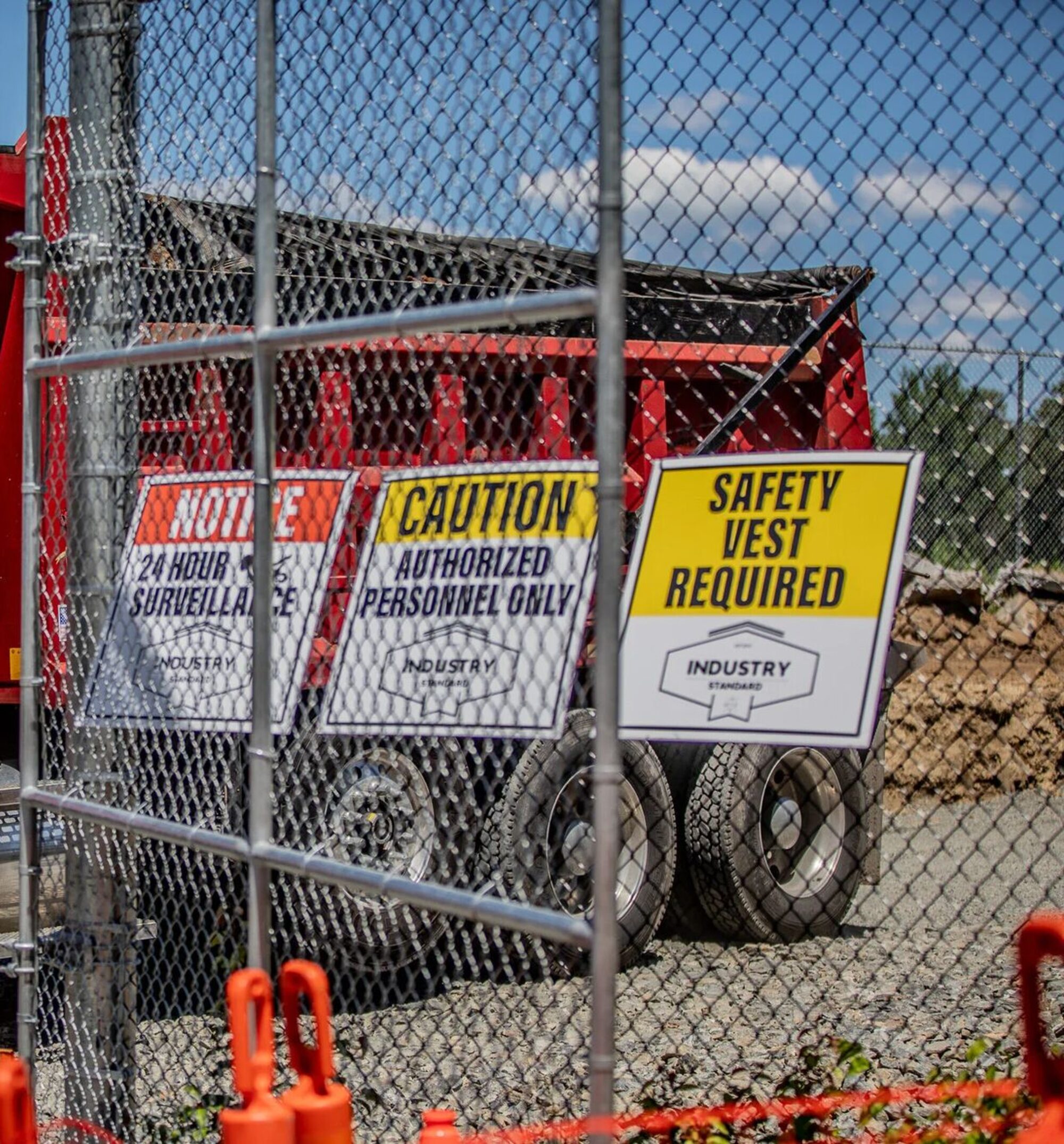 An Industry Standard USA jobsite perimeter with branded notice, caution, and safety vest signage in front of a loaded dump truck